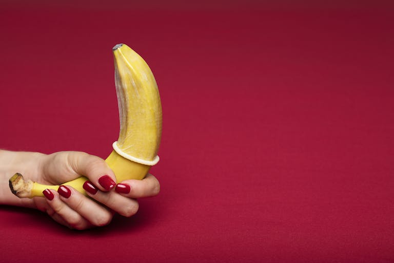 Creative representation of safe sex using a banana with a condom against a red background.