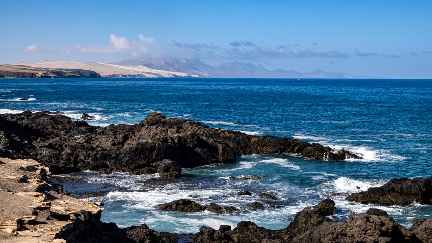 A stunning view of a rocky coastline with waves crashing against the shore under a clear blue sky.