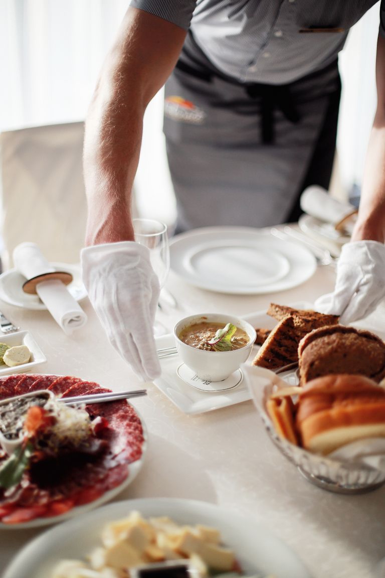 Waiter setting an elegant restaurant table with dishes and bread.