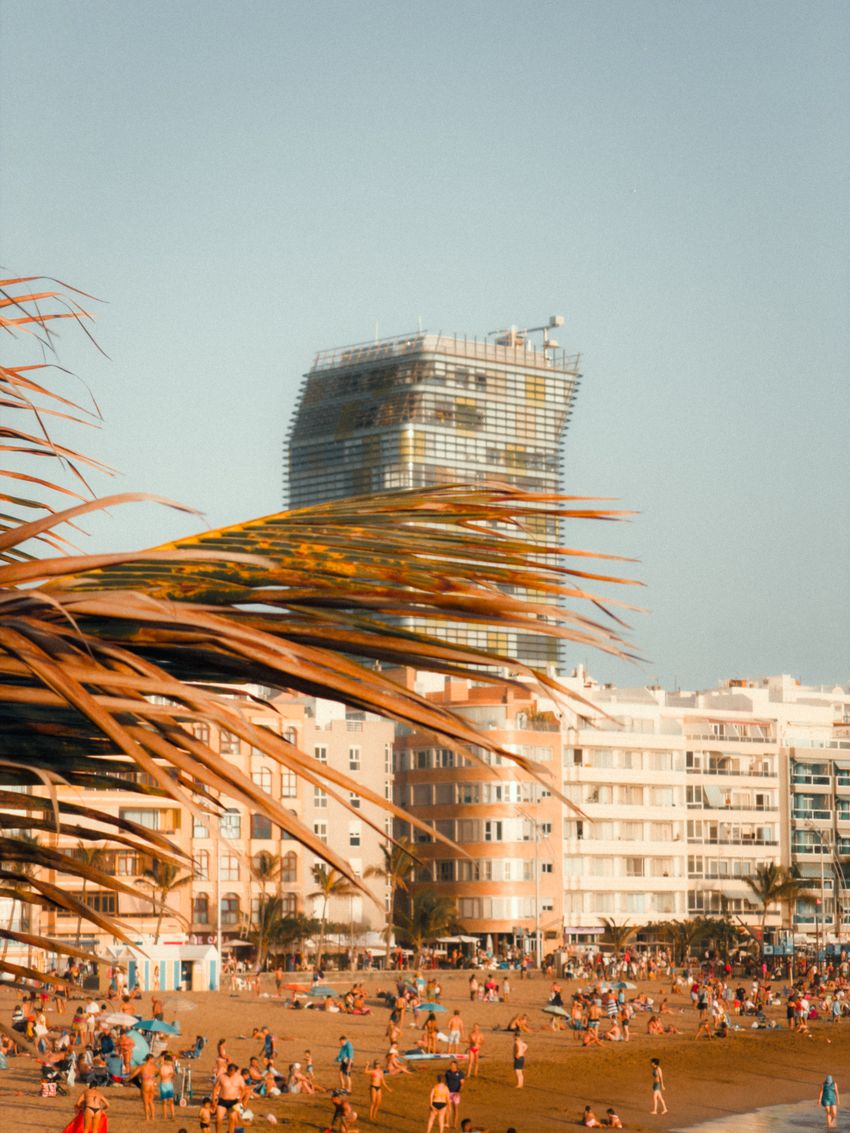 Vibrant summer day at Las Palmas beach with a prominent skyscraper in view.